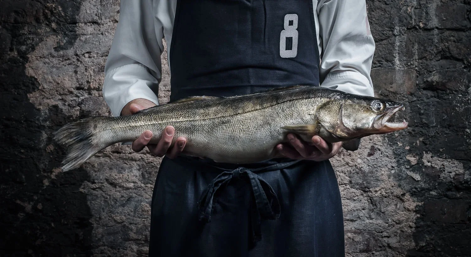 Chef holding a large fresh fish in a professional kitchen.